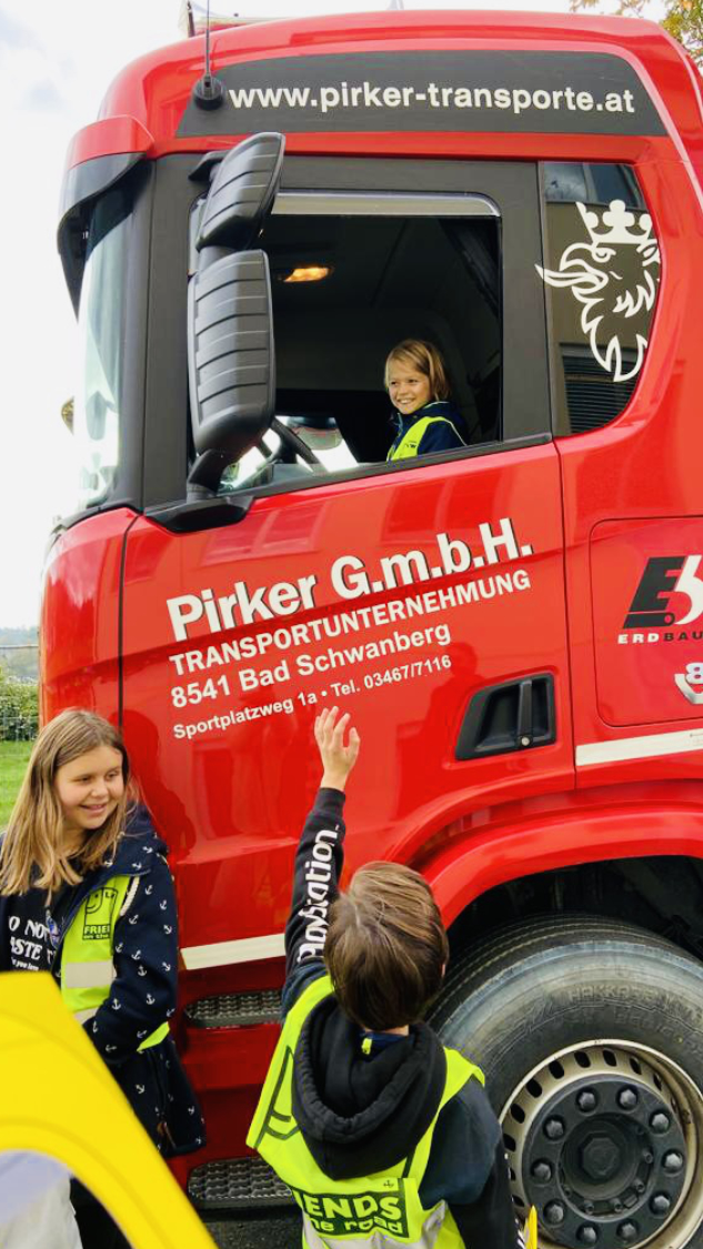 Roter LKW in dem ein Mädchen sitzt und unten mehrere Kinder stehen