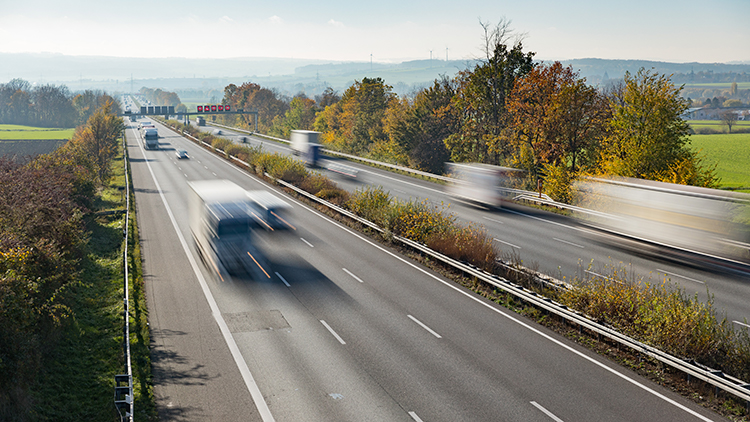Autobahn in Vogelperspektive mit bewegungsunscharfen Fahrzeugen umgeben von gr&uuml;ner Landschaft