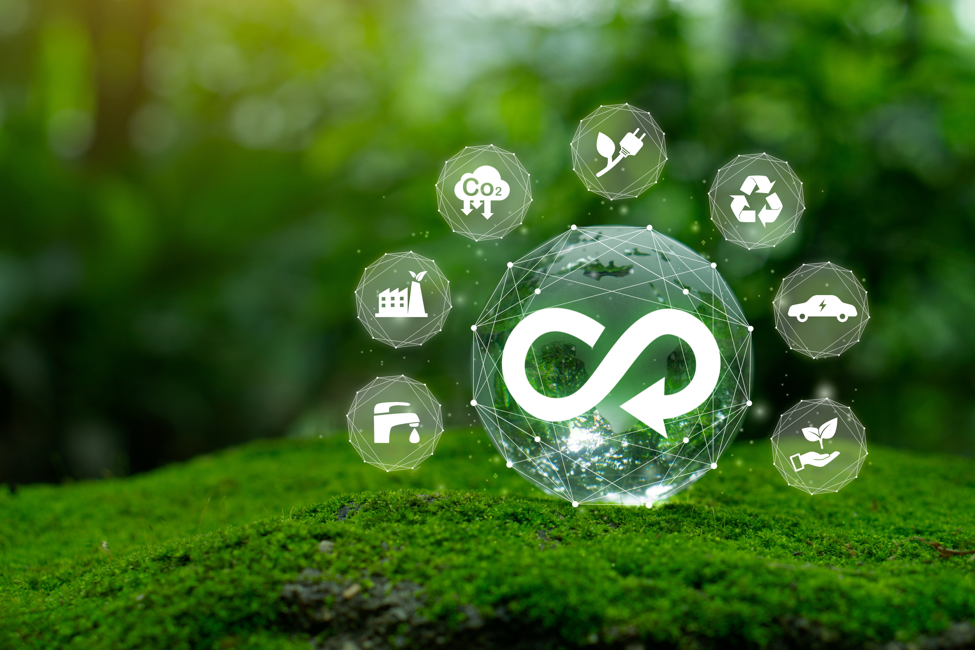 Gerenderte Kugel auf Moos bestehend aus in Punkten zusammenlaufenden Linien mit wei&szlig;em Unendlichkeitssymbol mit Pfeil mittig, ringsum kleinere Kugeln mit Symbolen zum Thema Nachhaltigkeit wie Wasserh&auml;hne und Fabriksgeb&auml;ude aus dem ein Blatt ragt