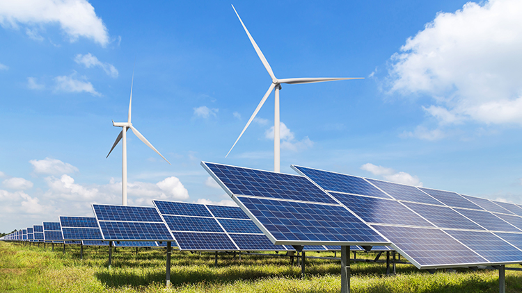 Windr&auml;nder und Photovoltaikpanele auf gr&uuml;ner Wiese, blauer Himmel im Hintergrund