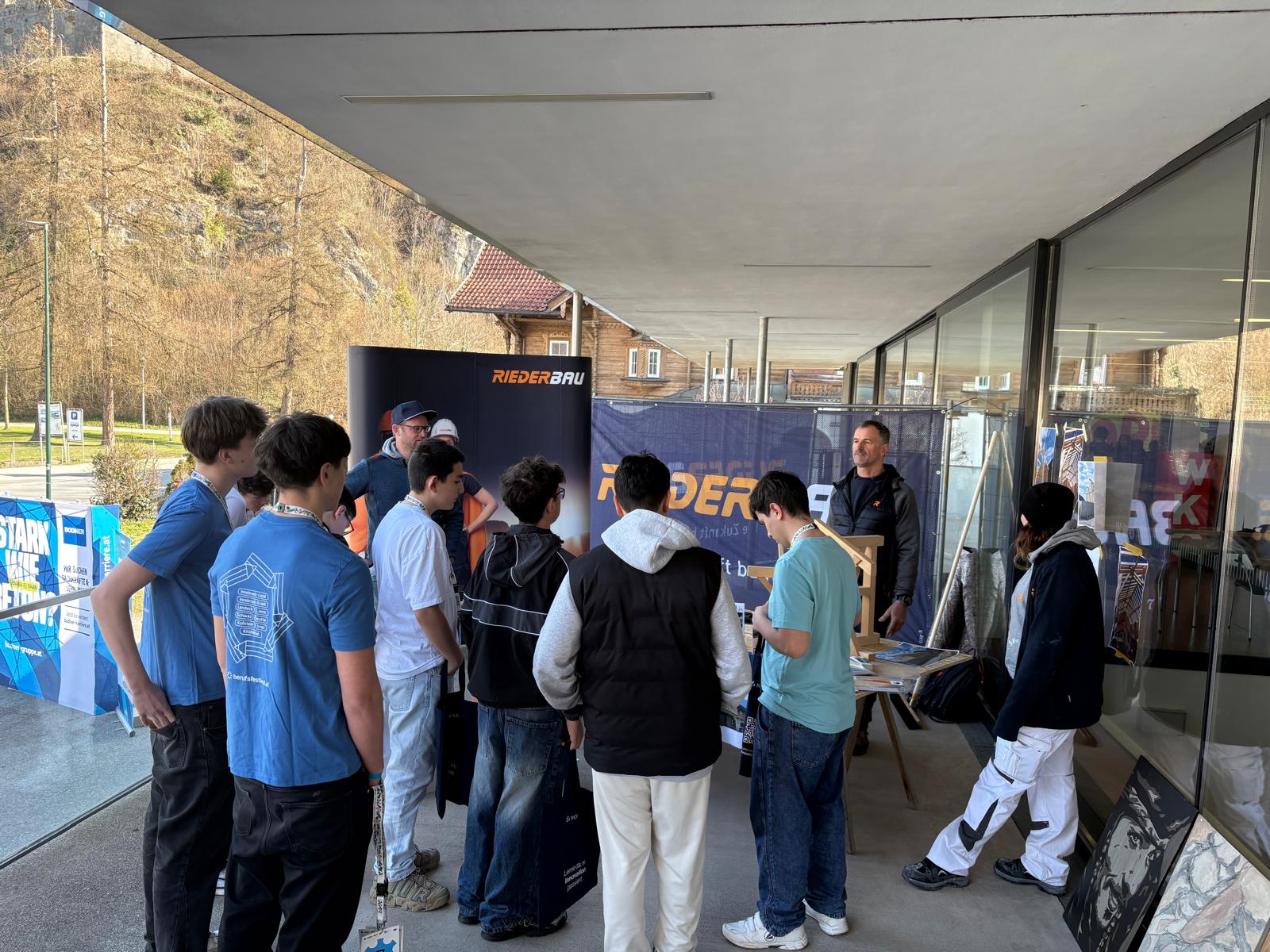 Sch&uuml;ler stehen im Freien um einen Stand eines Bauunternehmens und erhalten Einblicke in praktische T&auml;tigkeiten beim Berufsfestival Kufstein.
