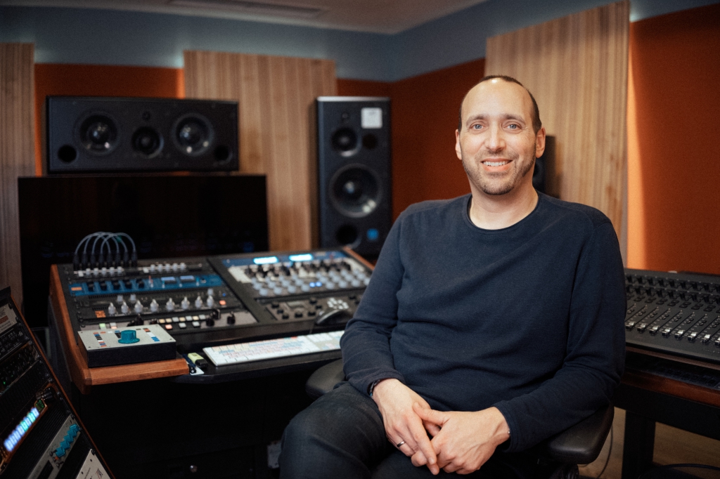Person sitzt vor Mischpult und Studiotechnik in einem Tonstudio.