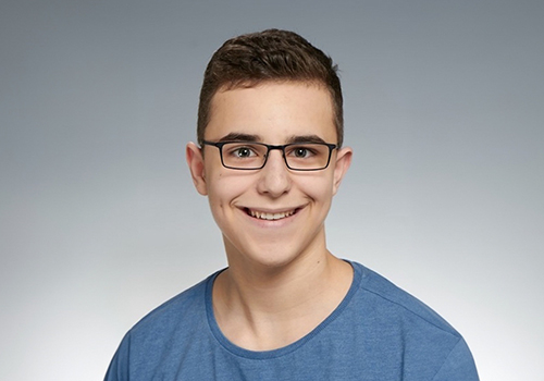 Person mit Brille blickt in die Kamera, l&auml;chelt. 