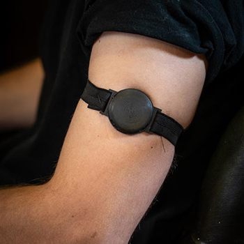 Oberarm einer Person mit einem schwarzen Armband, an dem ein runder Sensor befestigt ist.