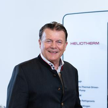 Person in dunkler Jacke steht lächelnd in einem hellen Raum neben einer Heliotherm-Wärmepumpe.