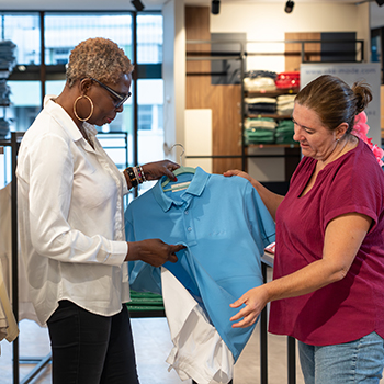 Zwei Personen in einem Bekleidungsgeschäft betrachten gemeinsam ein hellblaues Polohemd auf einem Kleiderbügel.