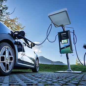 Schwarzes Elektroauto lädt an einer modernen Ladesäule im Freien vor Bergkulisse und blauem Himmel.