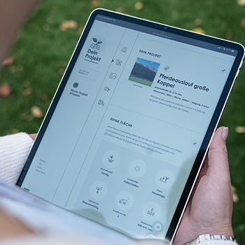 Person hält ein Tablet mit geöffneter Projektverwaltungs-App im Freien, im Hintergrund ist Rasen zu sehen.