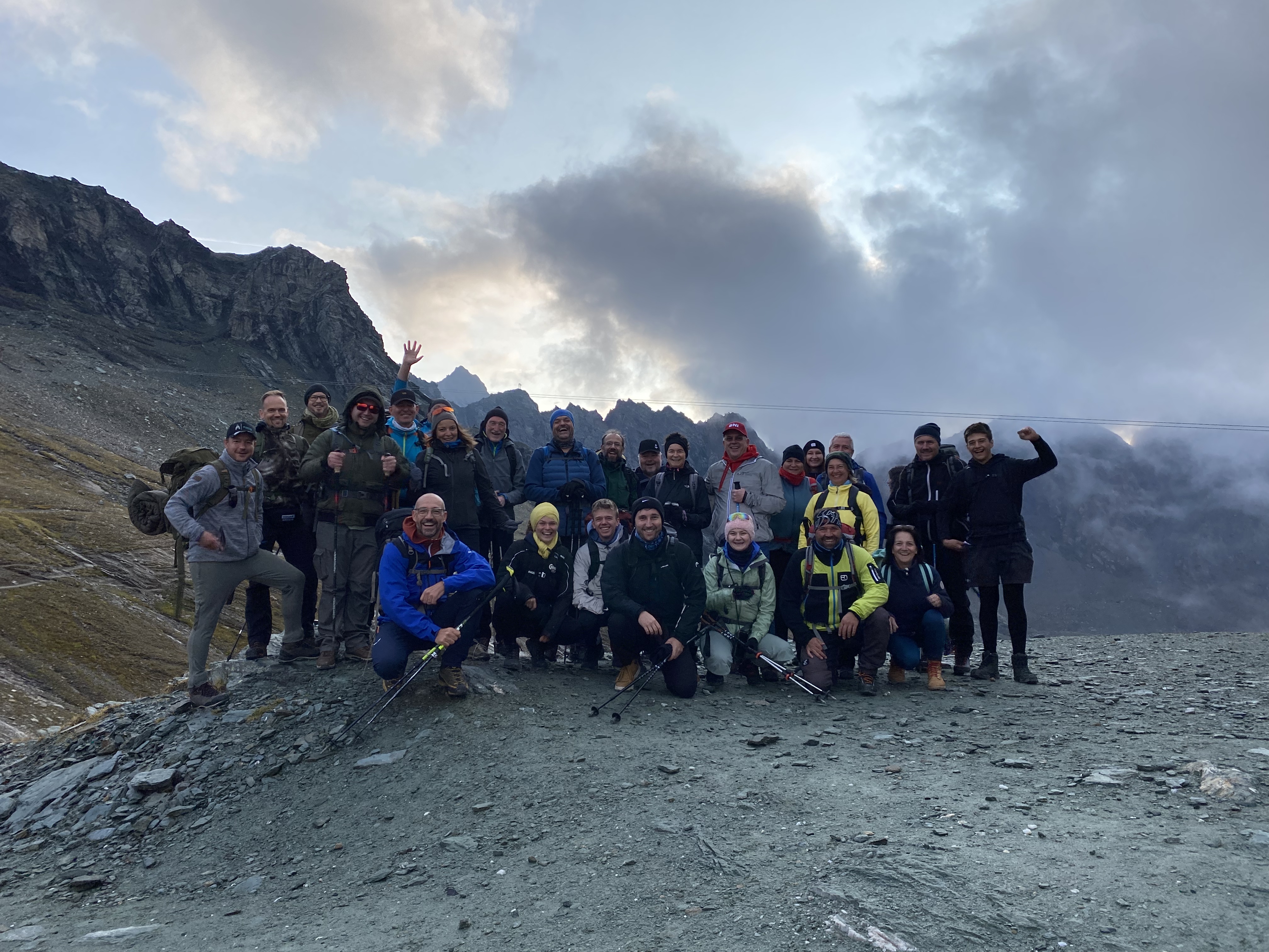 Eine Gruppe von Menschen in Wanderkleidung posiert in einer alpinen Berglandschaft f&uuml;r ein Gruppenfoto.