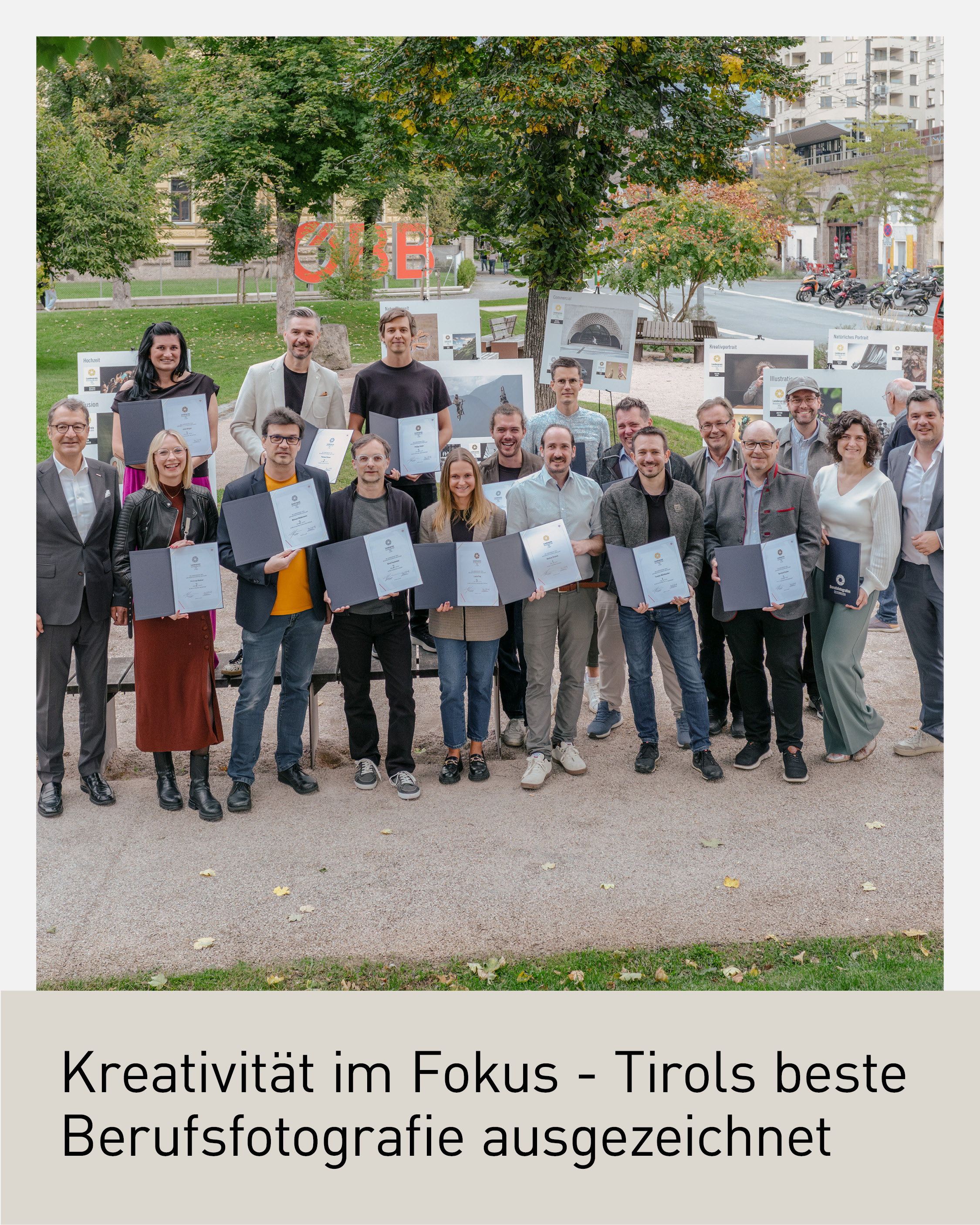 Gruppenfoto der zehn Gewinnerinnen und Gewinner des Tiroler Landespreises der Berufsfotografie 2025 mit Urkunden in Innsbruck, aufgenommen im Freien mit ausgestellten Fotografien im Hintergrund.