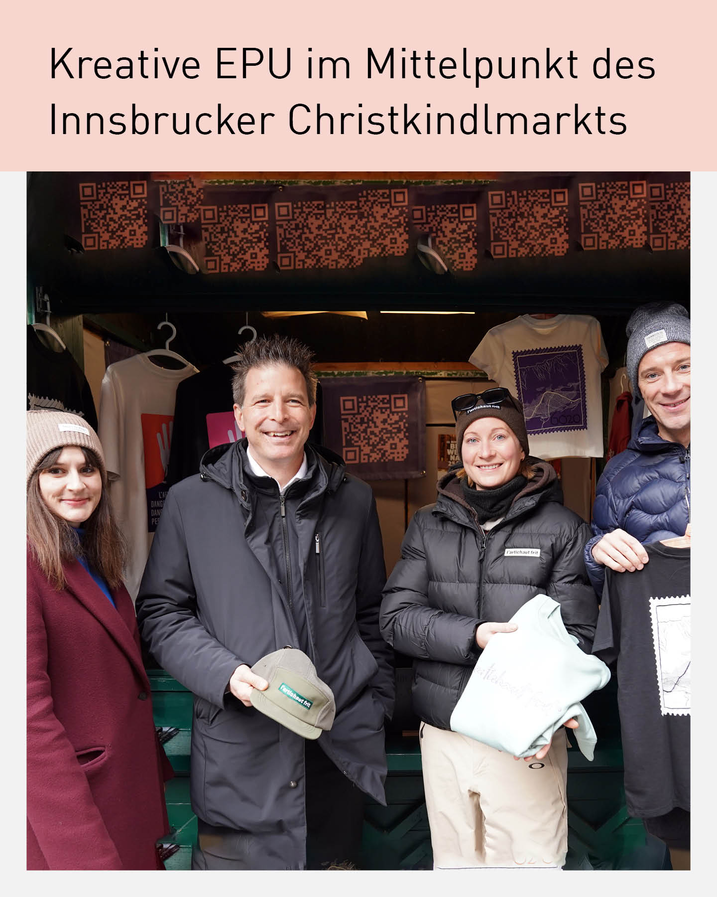 Gruppe von vier Personen vor dem EPU-Stand am Innsbrucker Christkindlmarkt; sie präsentieren handgemachte Produkte wie Kleidung und Accessoires. Der Marktstand im Hintergrund zeigt kreative Designs und T-Shirts, die Vielfalt und Innovationskraft von Ein-Personen-Unternehmen widerspiegeln.