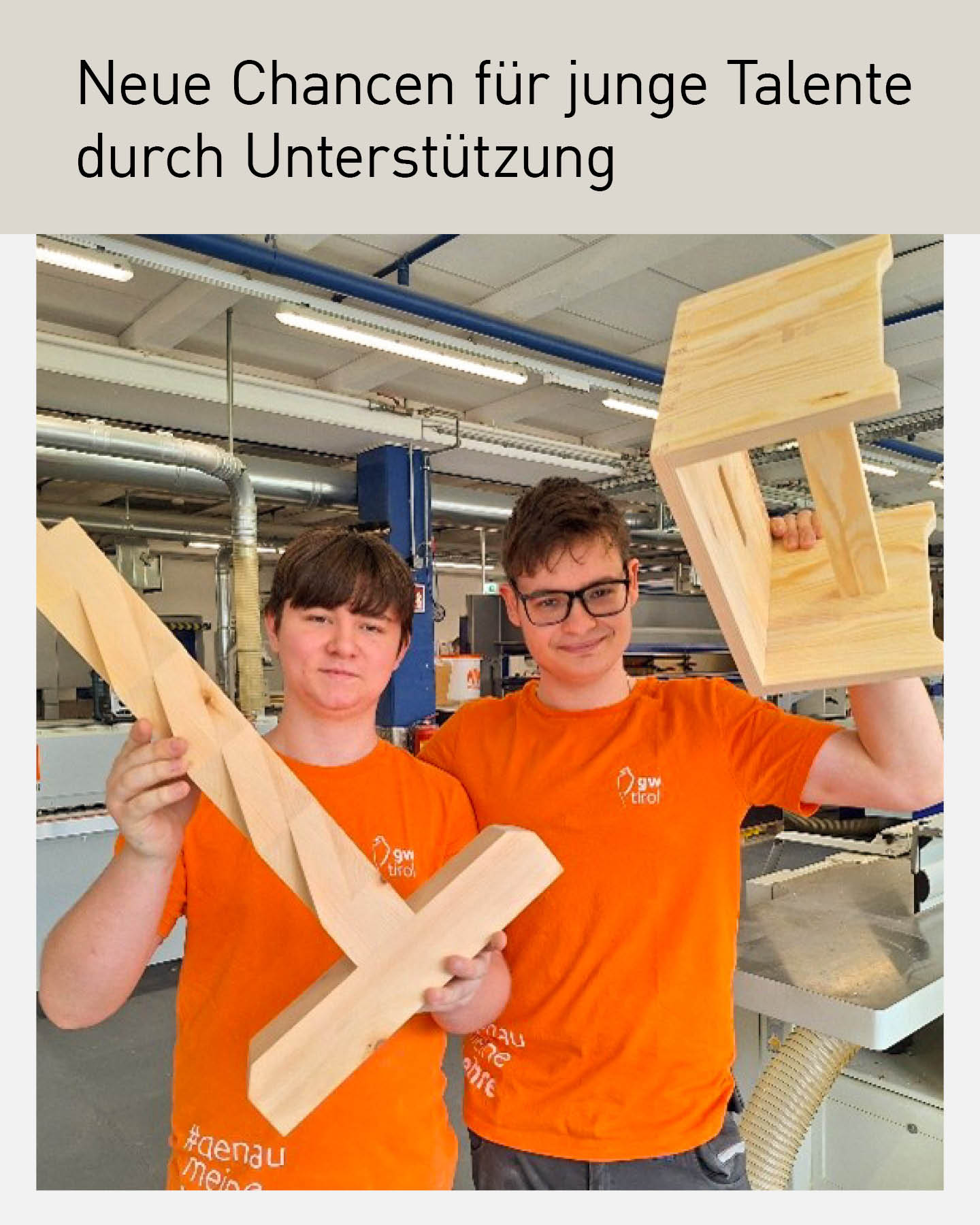 Zwei junge Auszubildende in orangefarbenen T-Shirts präsentieren stolz ihre selbst gefertigten Holzarbeiten in einer modernen Werkstatt. Beide lächeln in die Kamera und zeigen handwerkliches Können im Ausbildungszentrum für Jugendliche mit Behinderungen in Tirol.