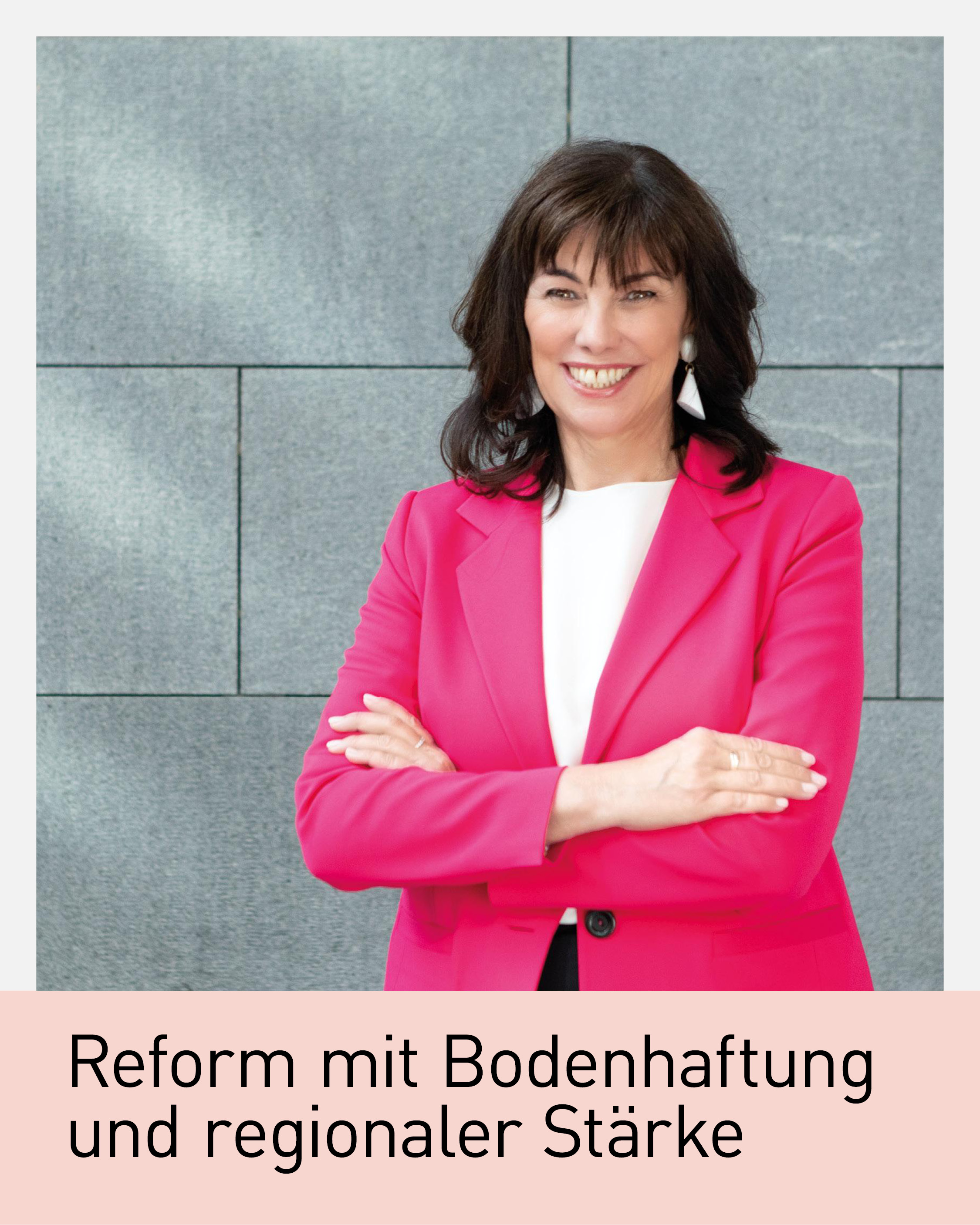 Portr&auml;t von Martha Schultz, gesch&auml;ftsf&uuml;hrende Vizepr&auml;sidentin der Wirtschaftskammer &Ouml;sterreich, vor grauer Steinwand. Sie tr&auml;gt einen pinken Blazer, steht mit verschr&auml;nkten Armen und l&auml;chelt in die Kamera
