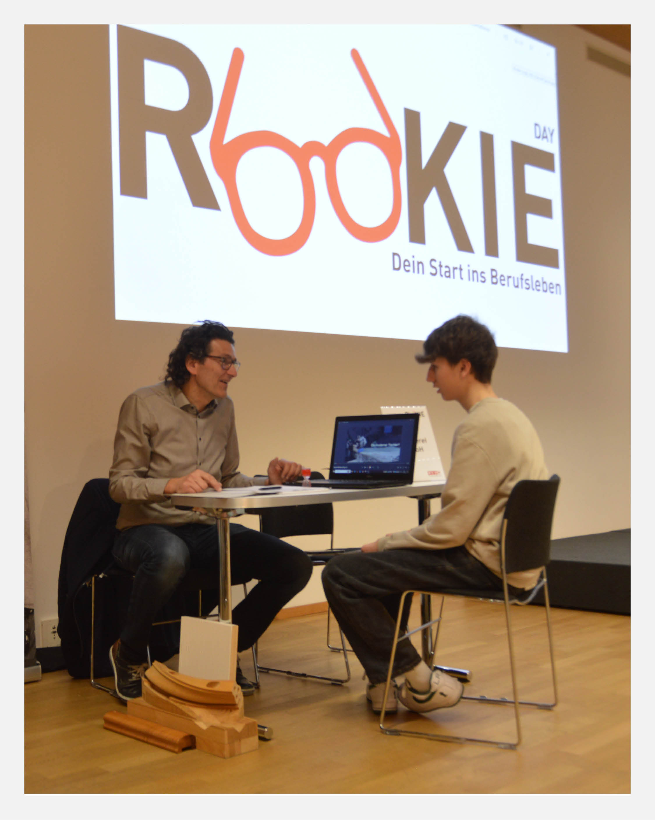 Rookie Day der Wirtschaftskammer Tirol in Innsbruck: Ein Sch&uuml;ler f&uuml;hrt ein 8-min&uuml;tiges Kennenlerngespr&auml;ch mit einem Unternehmensvertreter bei einem Tischgespr&auml;ch vor einer Pr&auml;sentationswand mit dem Rookie Day Logo. Die Veranstaltung bringt Jugendliche, Lehrbetriebe und Unternehmen zusammen und unterst&uuml;tzt Berufsorientierung, Lehrstellenvermittlung und Fachkr&auml;fteentwicklung in Tirol.