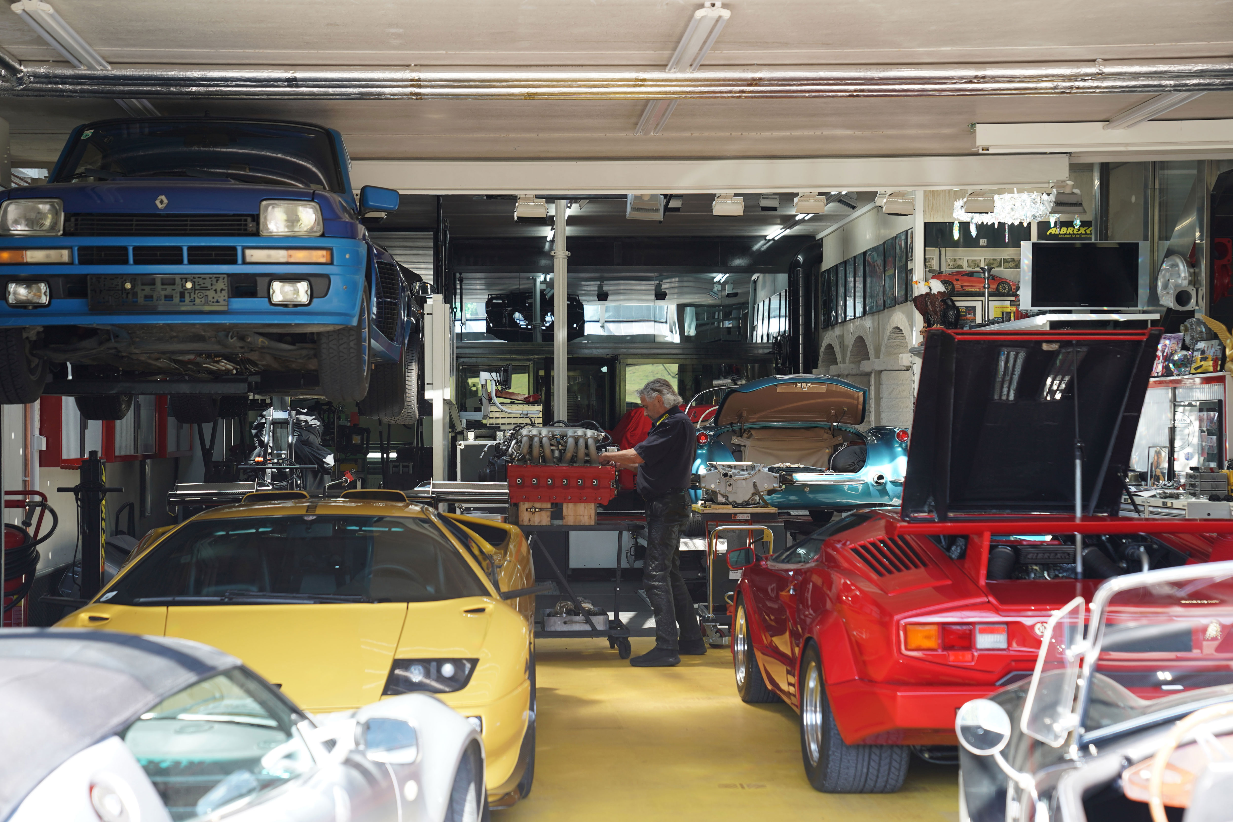 Blick in die Werkstatt von Albrex in Thierbach mit mehreren Sportwagen und Conrad Gruber bei der Arbeit an einem Hochleistungsmotor.