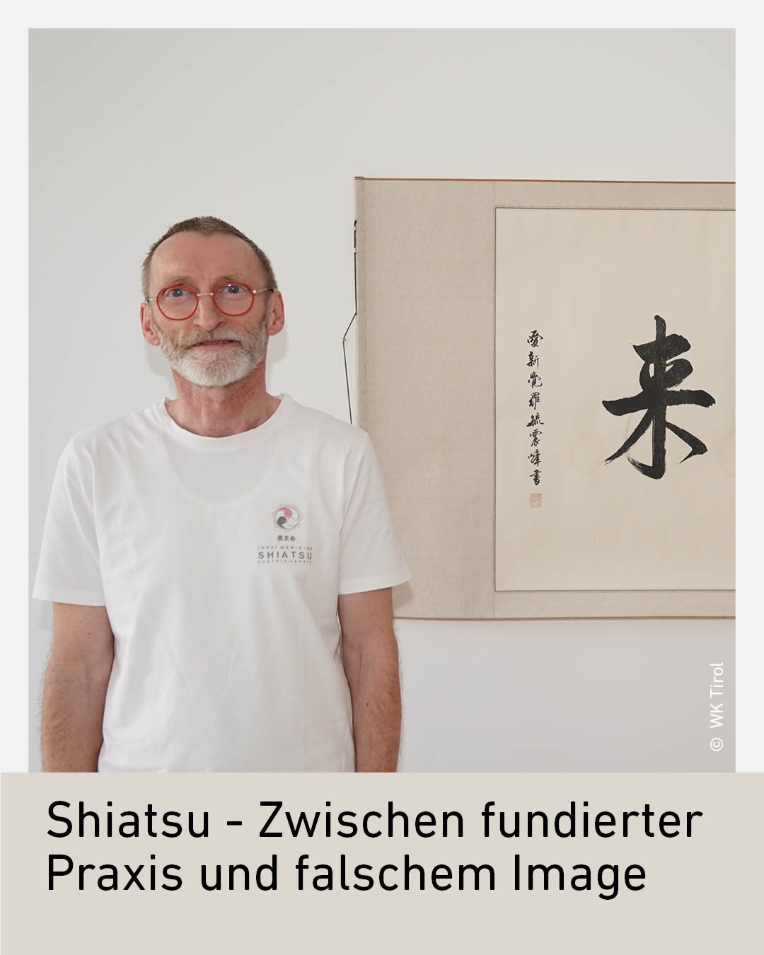 Ein Mann mit wei&szlig;em Bart und Brille steht vor einem japanischen Kalligraphie-Werk.