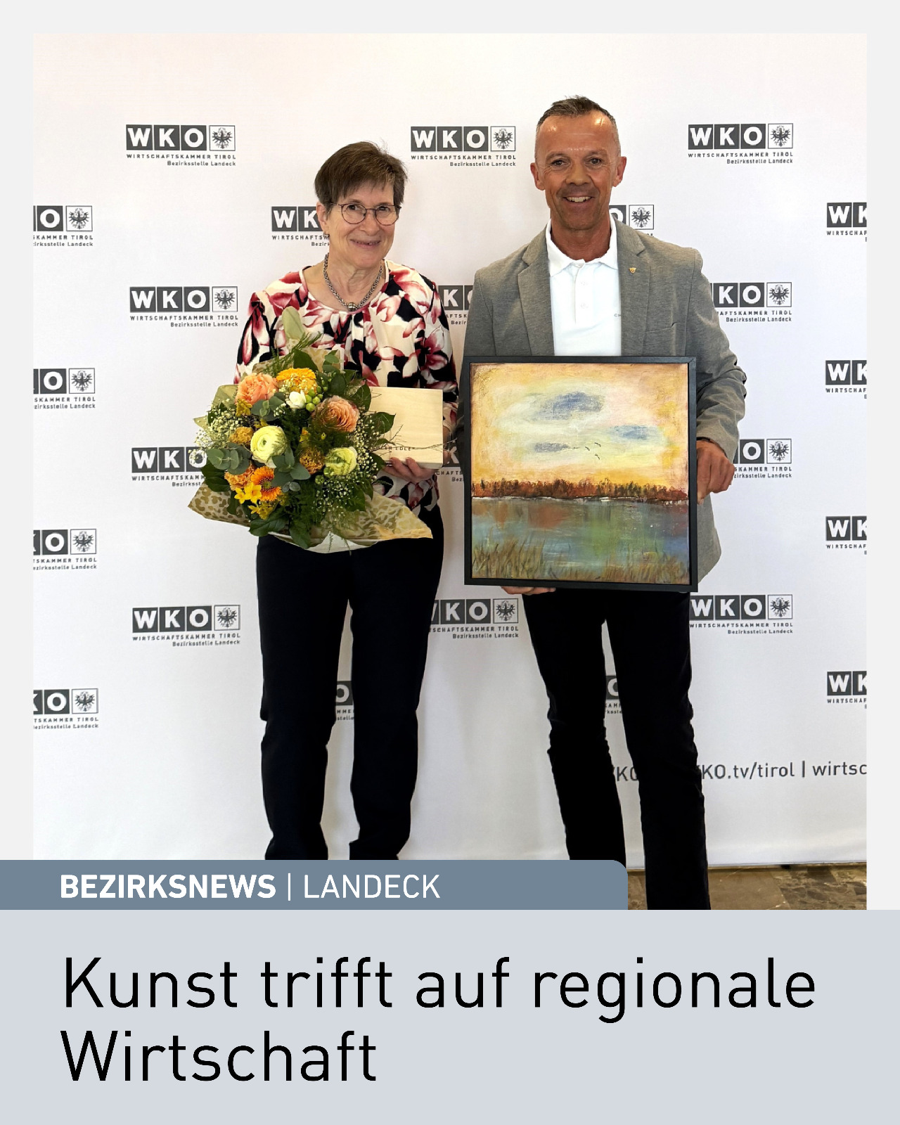 Frau und Mann pr&auml;sentieren Gem&auml;lde und Blumenstrau&szlig; bei Ausstellungser&ouml;ffnung in der Wirtschaftskammer Tirol Bezirksstelle Landeck, K&uuml;nstlerecke mit Acrylarbeiten von Veronika Tilg, regionale Kunst und Wirtschaft Tirol