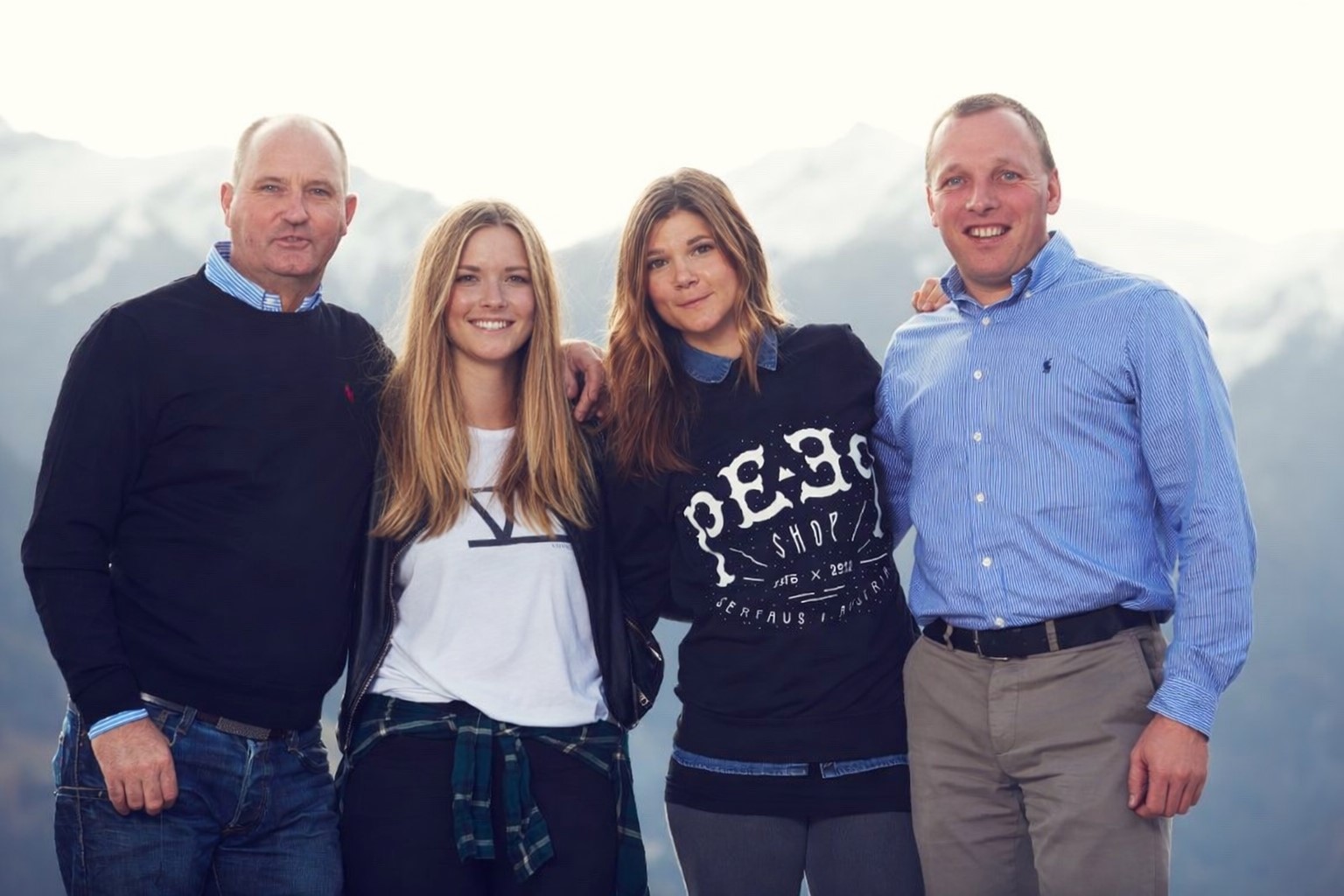 Vier Personen stehen nebeneinander im Freien vor einer Berglandschaft. Die Personen haben die Arme teilweise umeinander gelegt und blicken l&auml;chelnd in die Kamera. Sie tragen Freizeitkleidung.