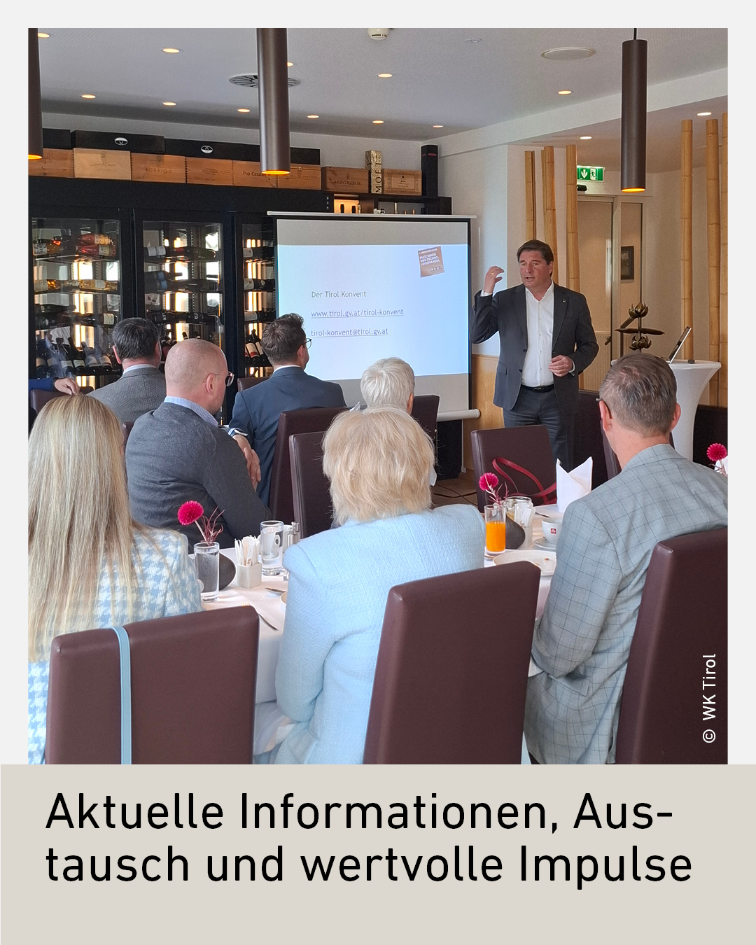 Eine Gruppe von Personen h&ouml;rt einem Mann zu, der eine Pr&auml;sentation vor einer Projektionsfl&auml;che h&auml;lt.