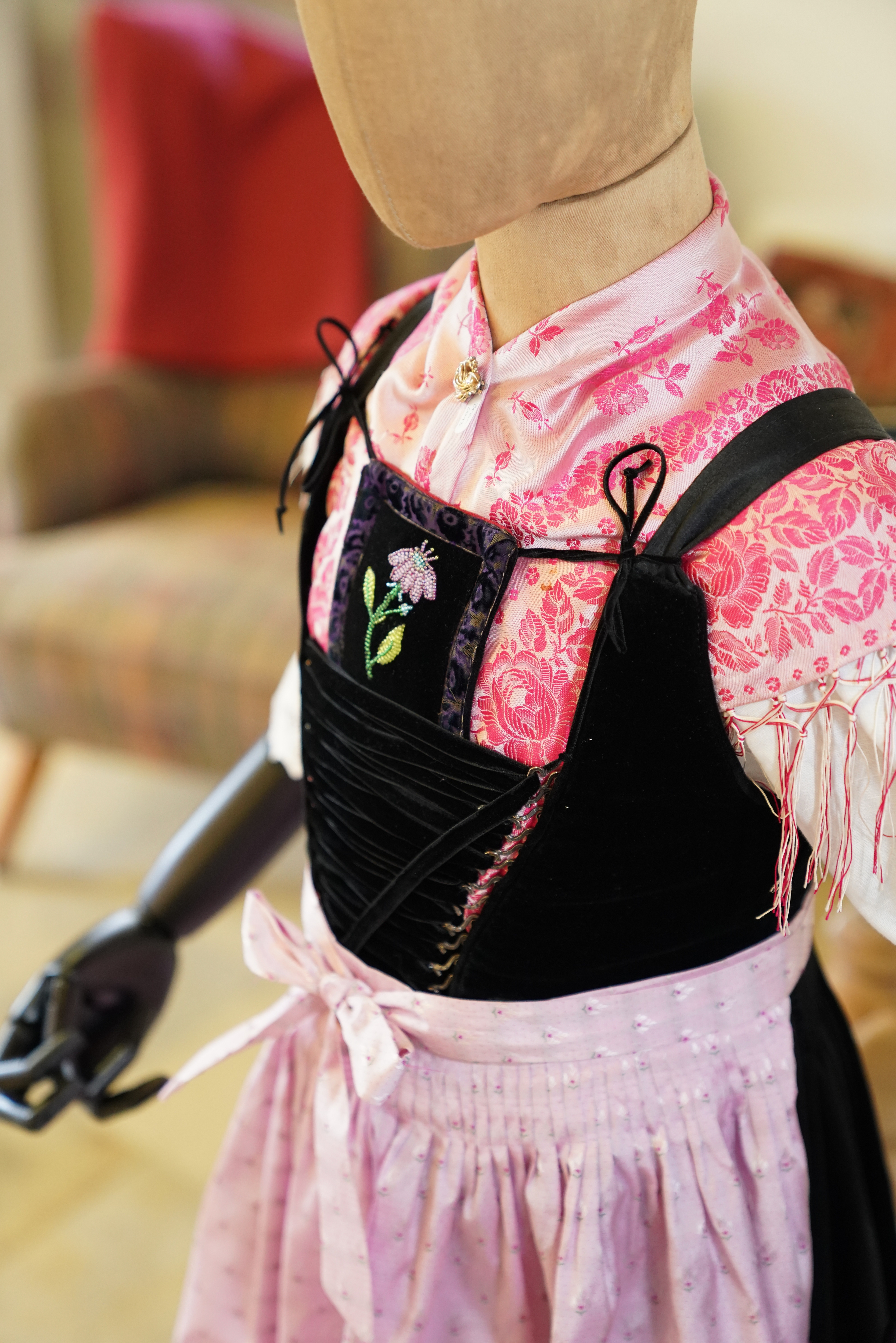 Eine Schneiderpuppe tr&auml;gt ein traditionelles Kleid mit rosa gemusterter Bluse, schwarzem Mieder und rosa Sch&uuml;rze. Das Mieder ist geschn&uuml;rt und mit einer kleinen Blumenstickerei verziert.