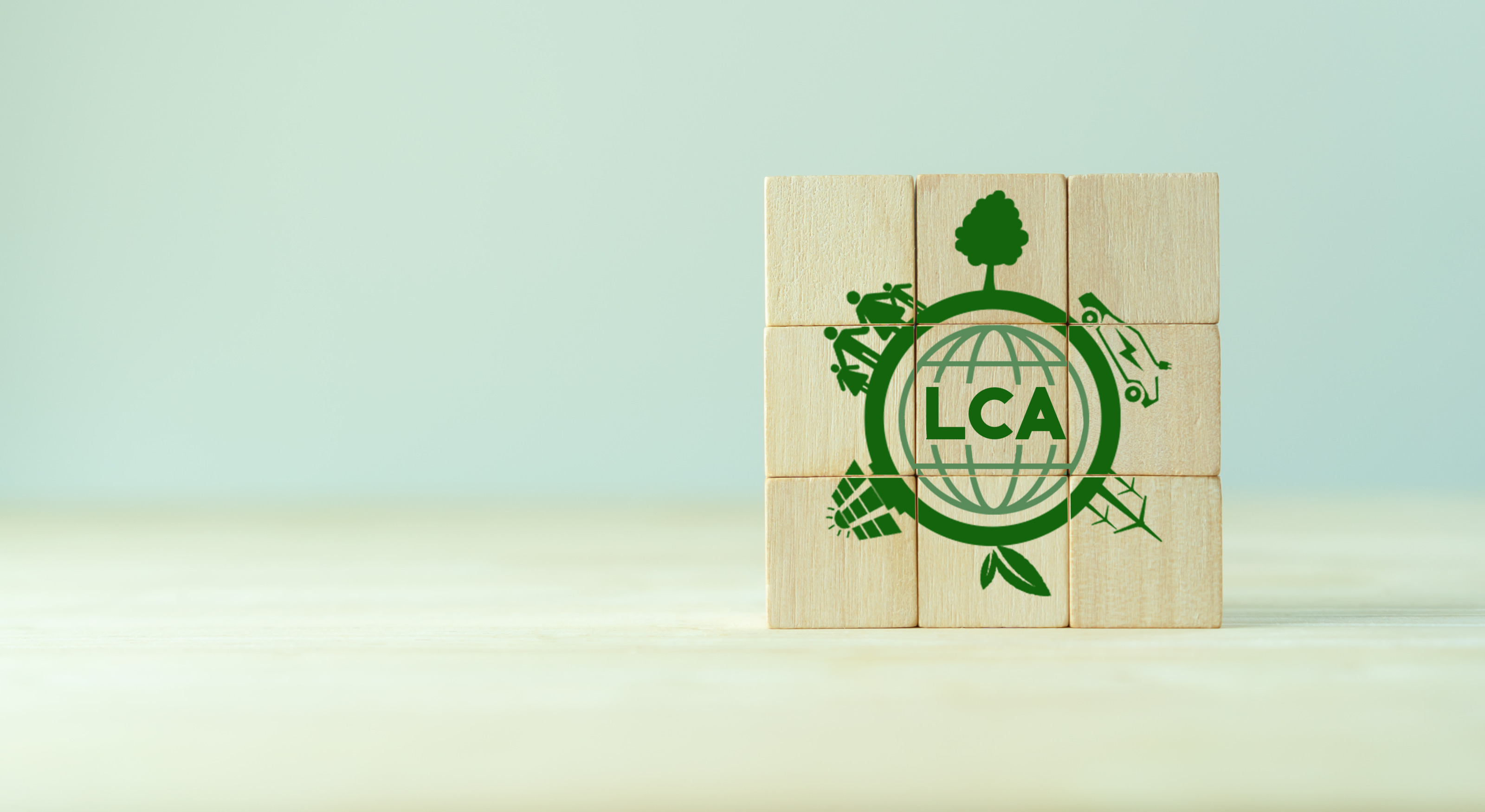 Neun Holzw&uuml;rfel in Dreierreihen &uuml;bereinander positioniert mit gr&uuml;nem Schriftzug LCA umrandet von Symbolen zur Nachhaltigkeit wie Windr&auml;der, Solaranlagen und Pflanzen.