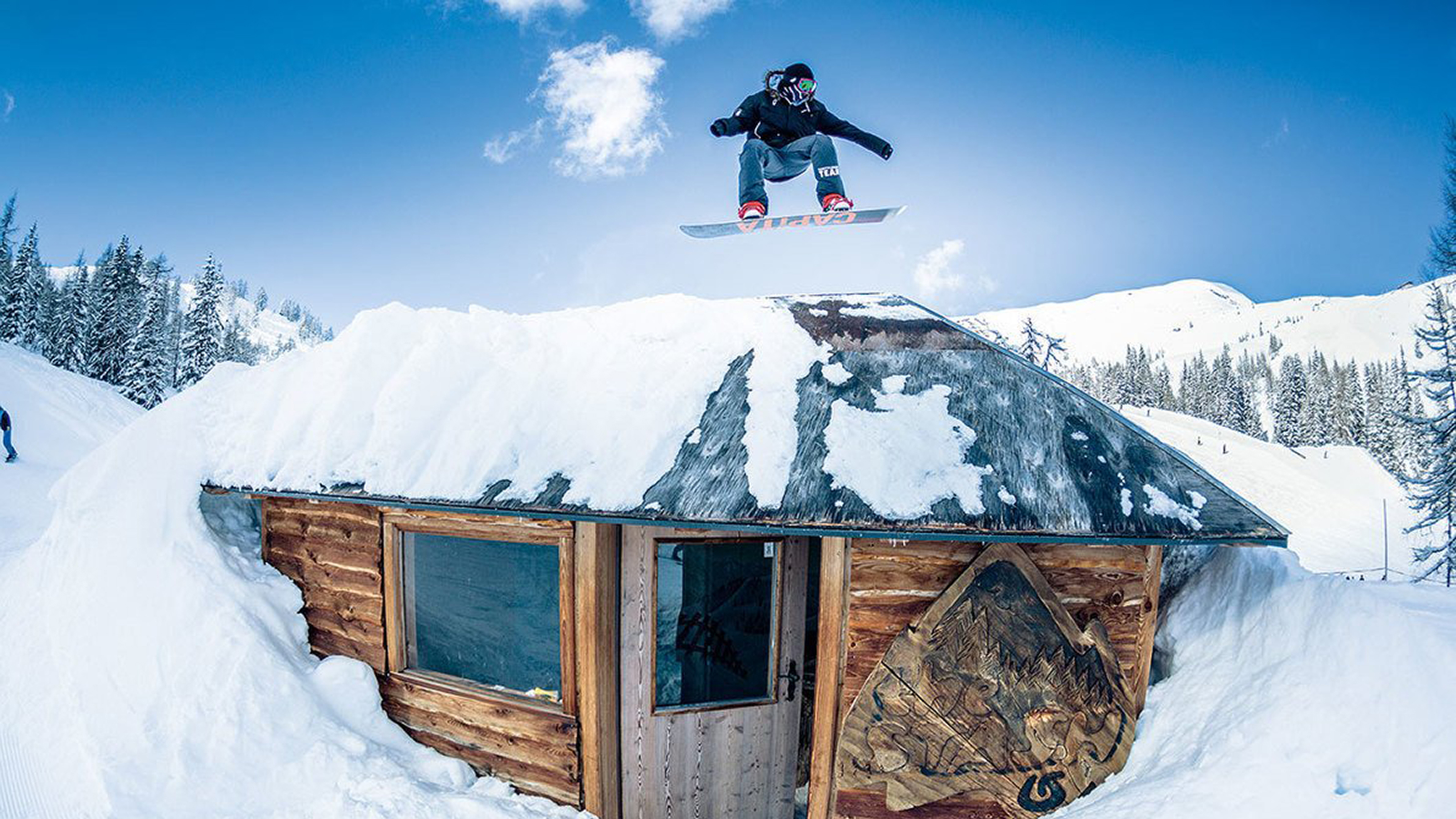 Snowboarder beim Sprung über eine Hütte