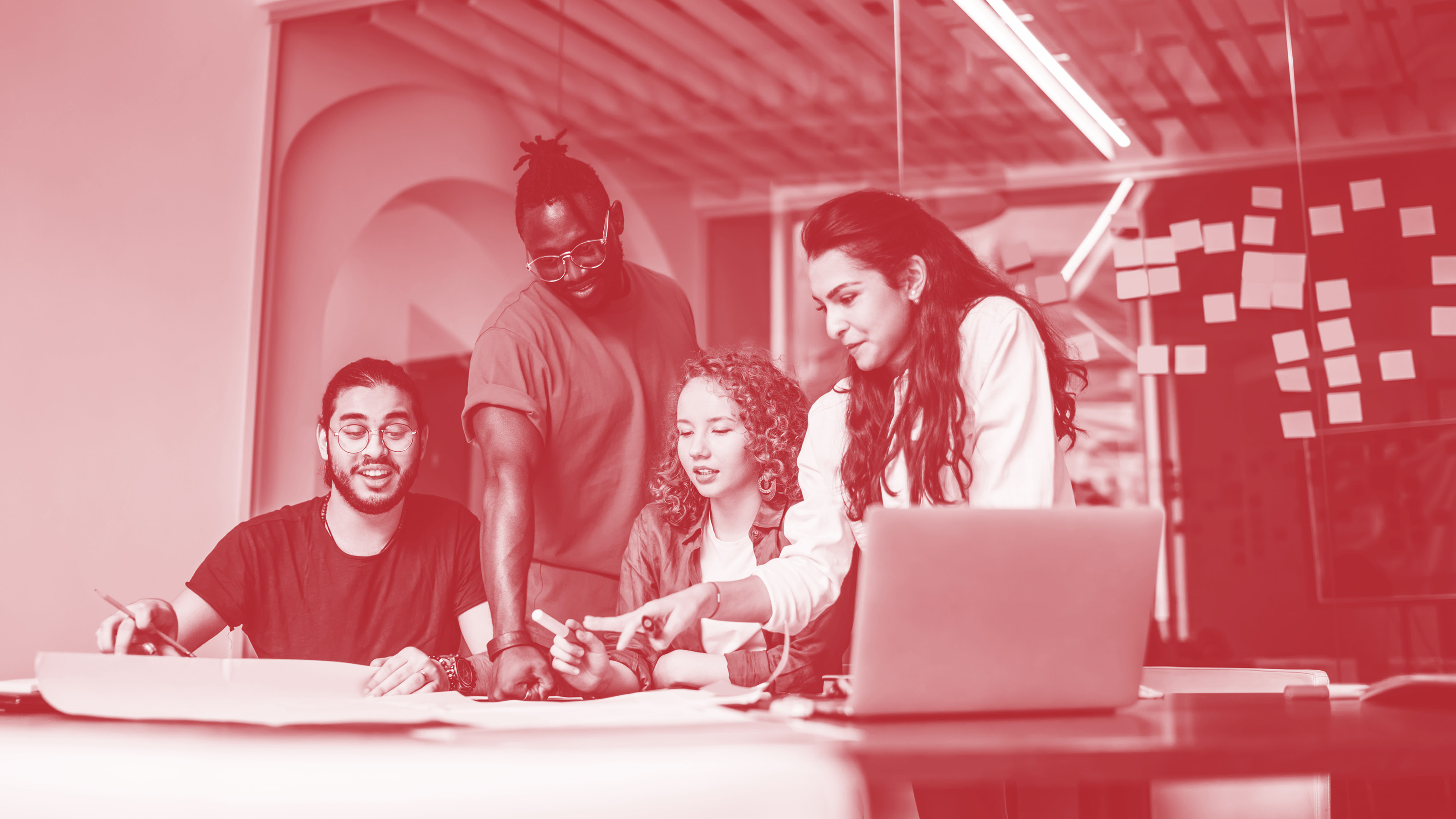 Junges fr&ouml;hliches Team bestehend aus zwei M&auml;nnern und zwei Frauen arbeitet gemeinsam an einem gro&szlig;en Glastisch mit Laptop