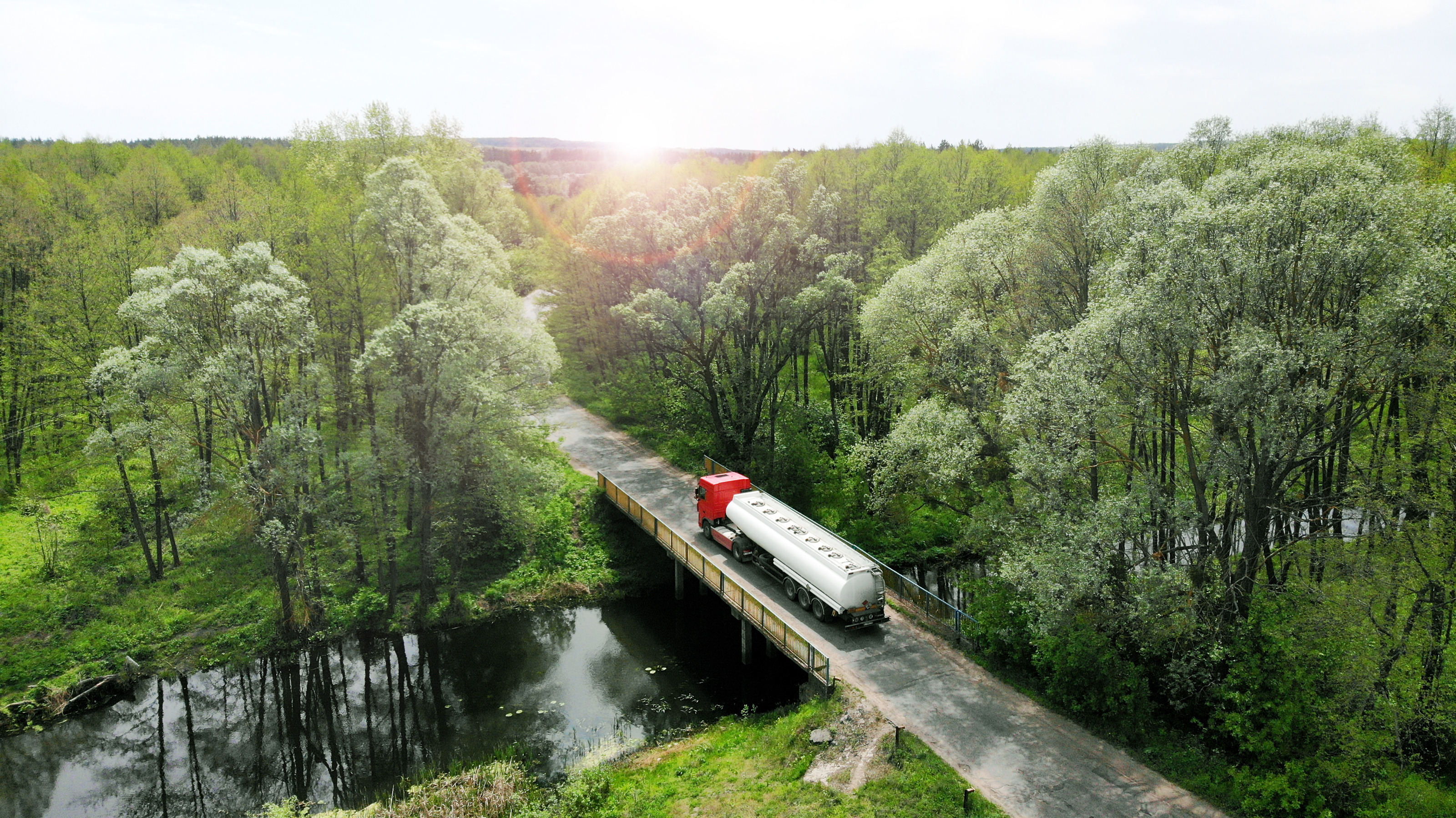 Aufnahme eines LKWs auf einer kleinen Br&uuml;cke aus der Vogelperspektive. Unter der Br&uuml;cke verl&auml;uft ein Fluss. Um die Br&uuml;cke und die Stra&szlig;e ist ein gr&uuml;ner Wald mit vielen B&auml;umen