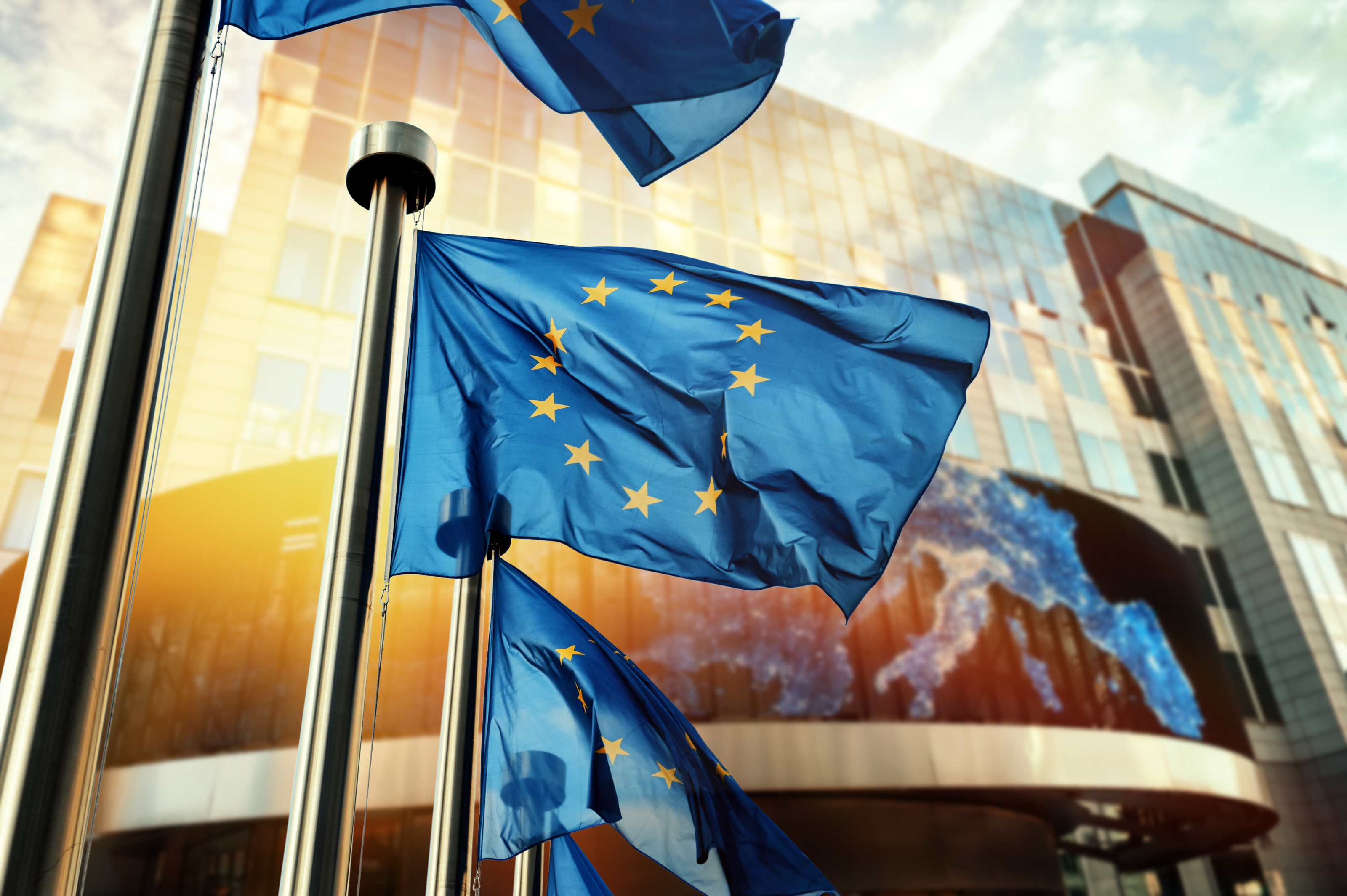 EU-Flagge in Wind wehen, im Hintergrund Glasfront eines Geb&auml;udes
