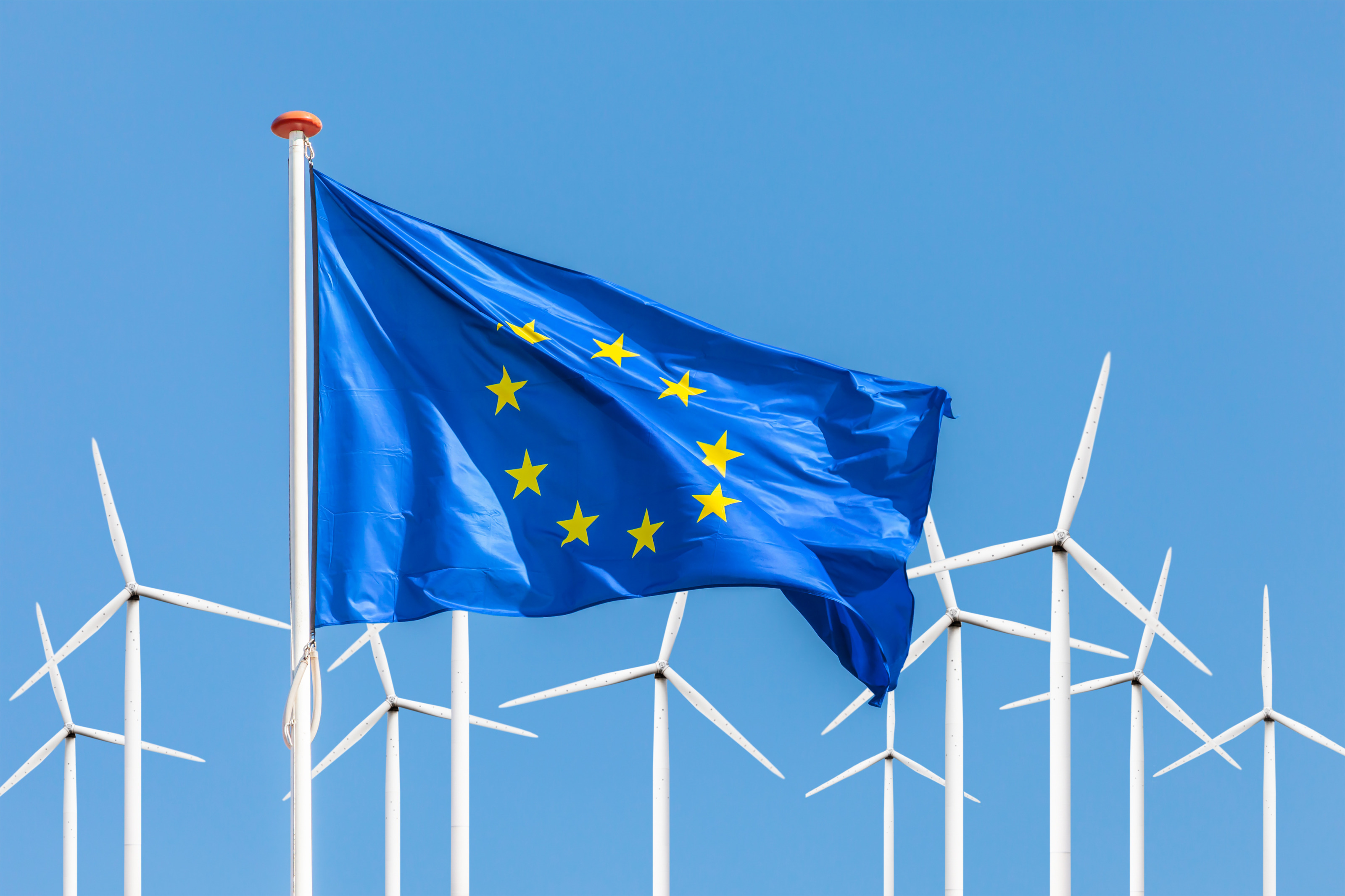 EU-Flagge im Wind wehend, im Hintergrund Windr&auml;der unter blauem Himmel