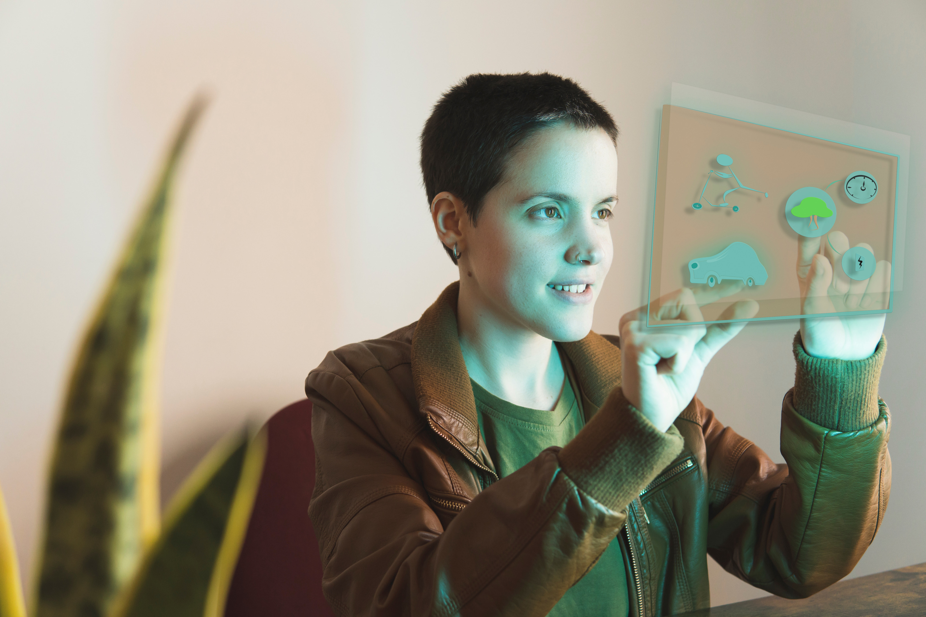 Sanft lächelnde Person mit Nasenpiercing hält beide Hände auf vor sich befindlichem grünblau leuchtendem Hologramm mit verschiedenen Grafiken: Baum, Uhr, Auto, Blitz und Figur auf Tretroller