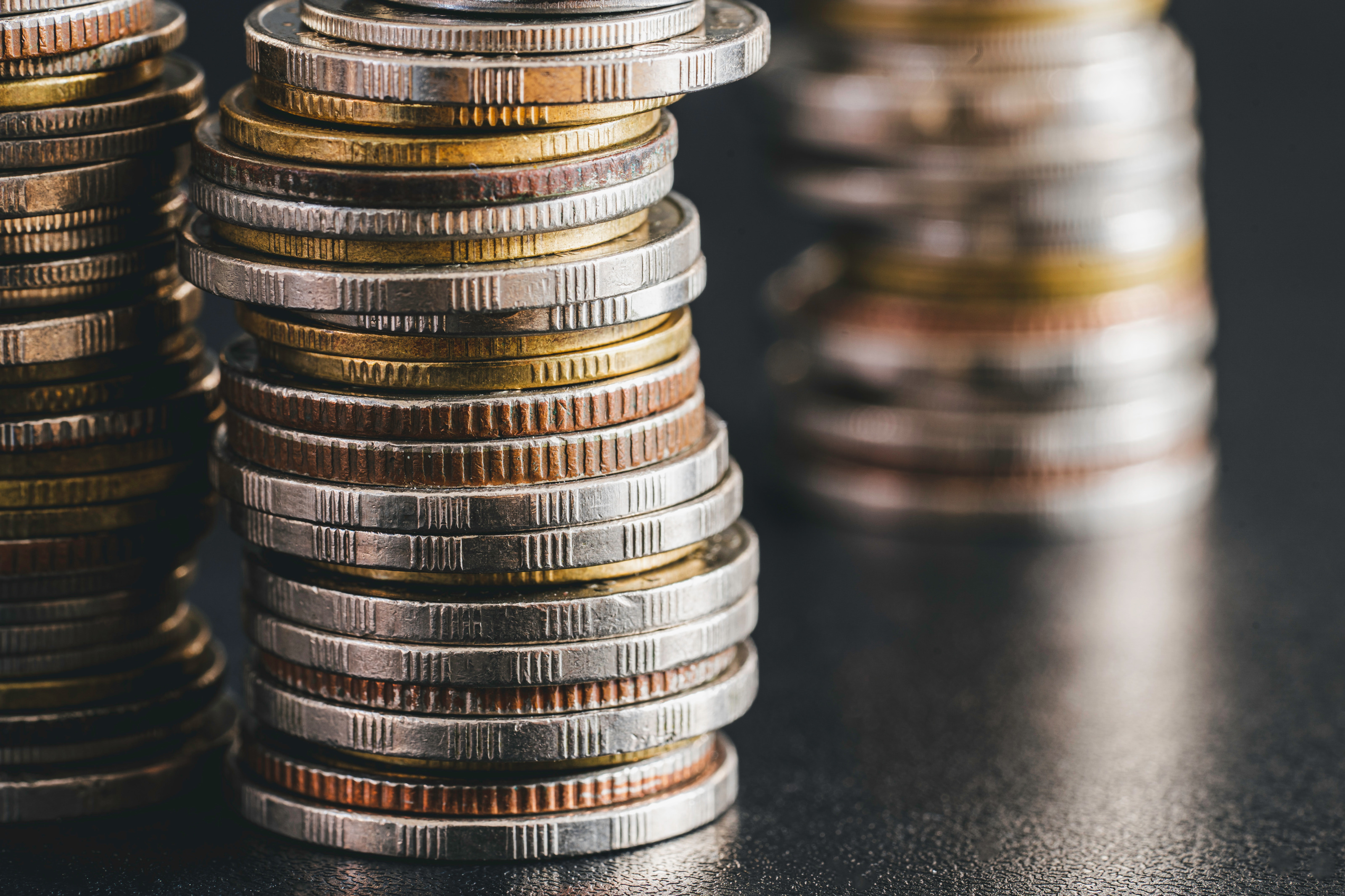 Nahaufnahme dreier Münzstapel auf einer dunklen Oberfläche.
