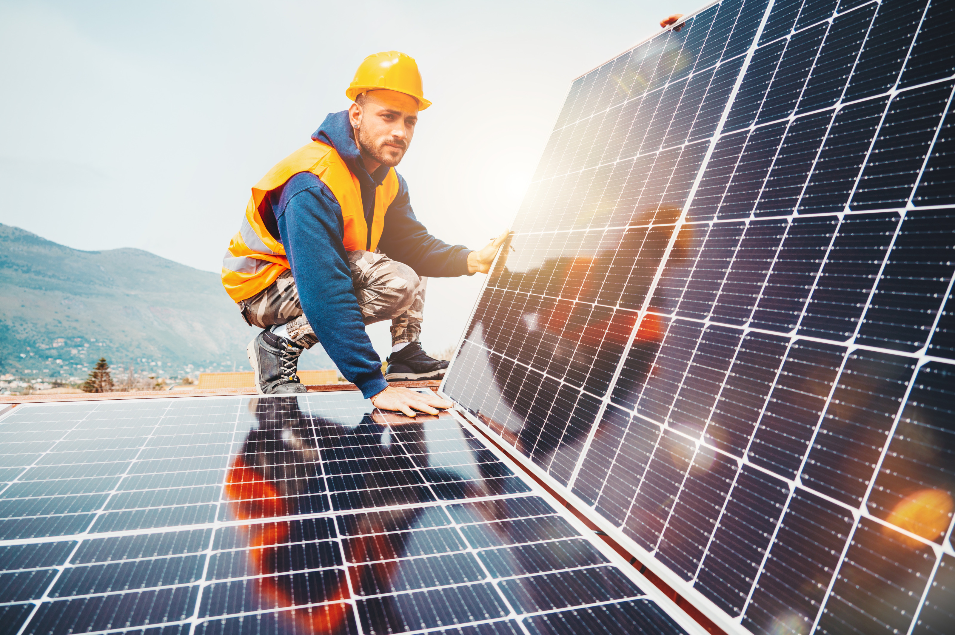 Person in Arbeitskleidung mit Schutzhelm und Warnweste montiert Solarpanele. 