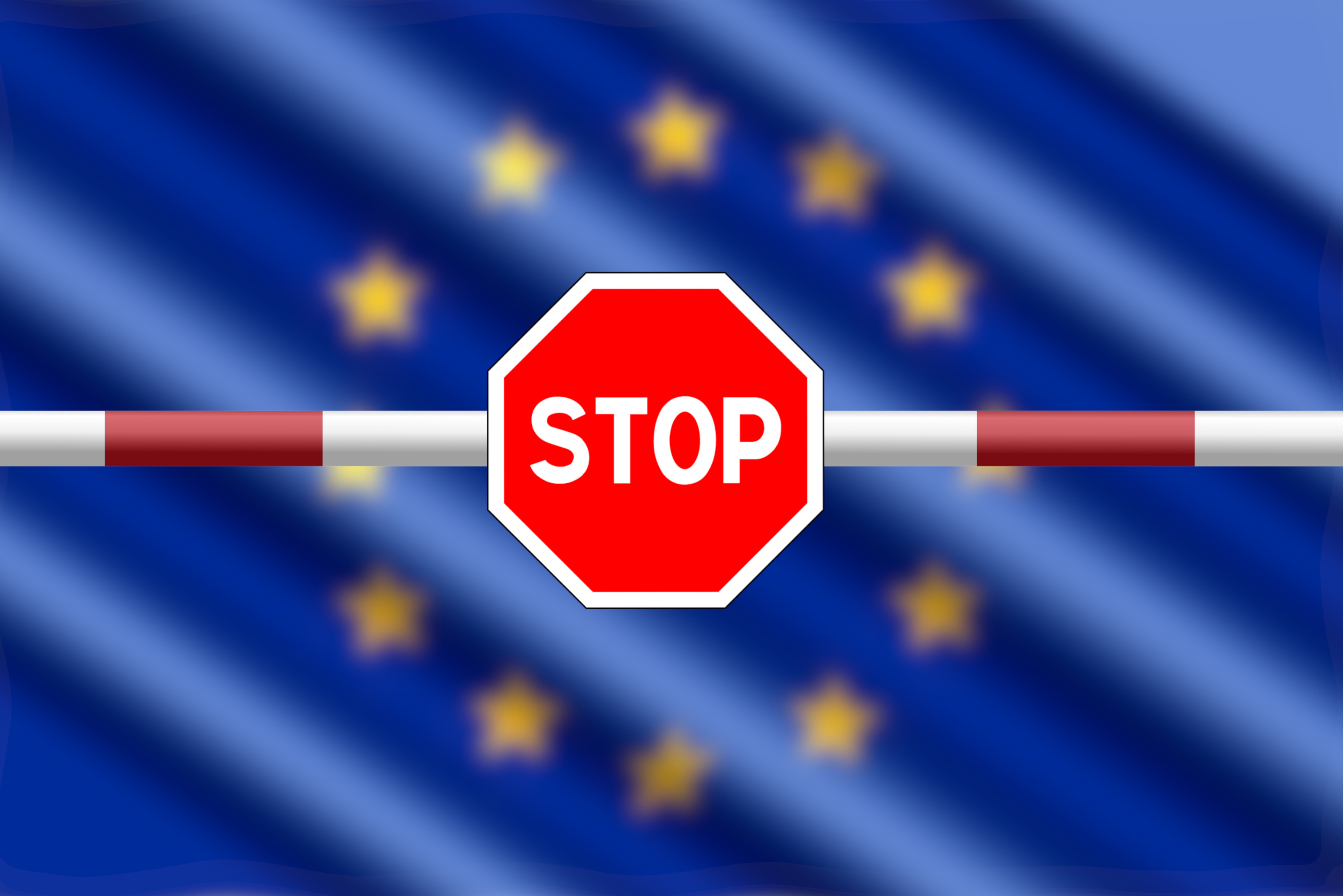 Ansicht eines Balken mit Stoppschild, im Hintergrund verschwommen die Flagge der europäischen Union.