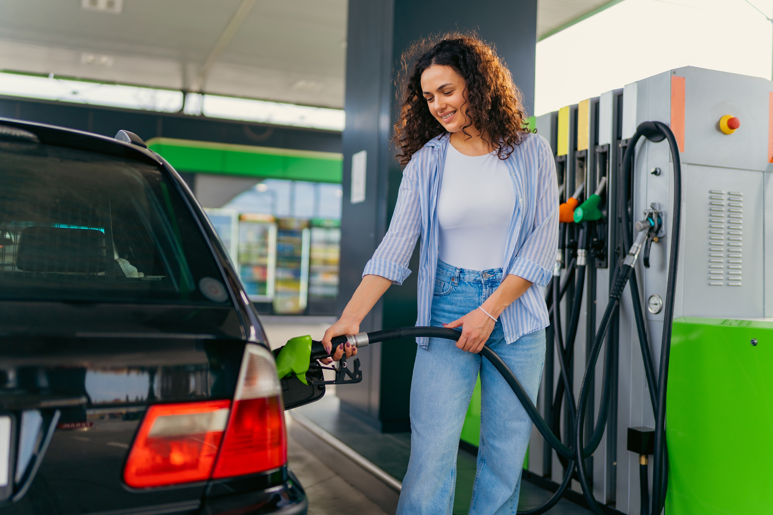 L&auml;chelnde Person steht auf Tankstelle und h&auml;lt Zapfhahn in Autotank